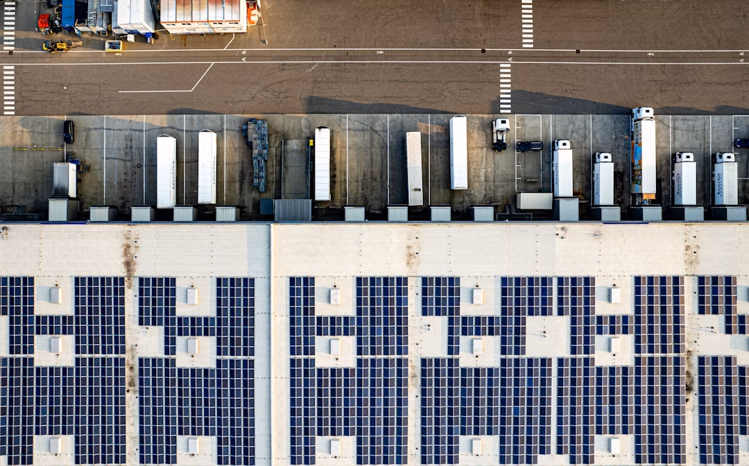sustainable automotive innovations driving the future — wide aerial shot of EV charging station hub with solar panels and multiple electric vehicles plugged in